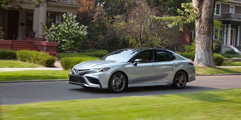 A silver Toyota Camry Hybrid is driving down a neighborhood road
