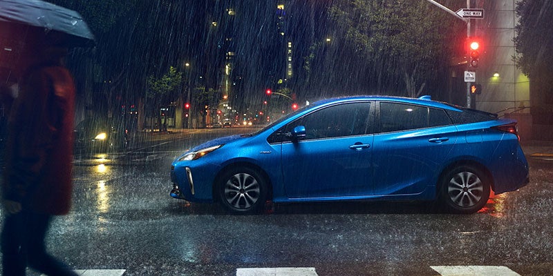 Side view of a blue 2021 Toyota Prius Prime driving through the city on a rainy night