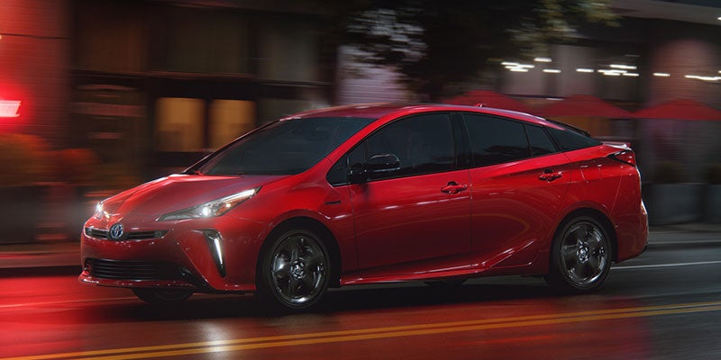 Side view of a red Toyota Prius driving down a city road at night