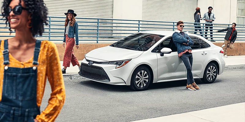 A 2022 Toyota Corolla Hybrid is parked on the side of the street with a man leaning on it
