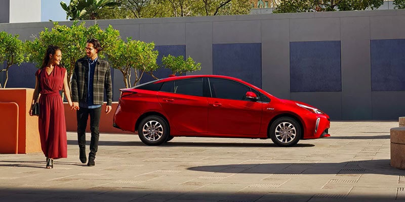A couple walks away from a red Toyota Prius parked on a city street.