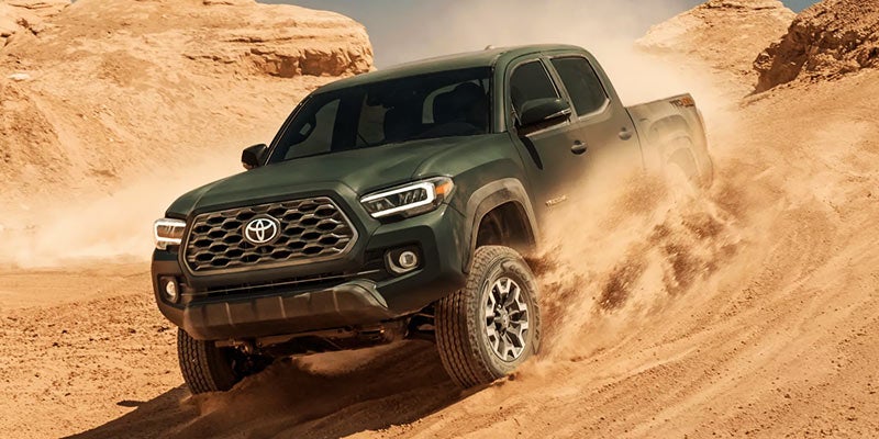 Front right view of a green Toyota Tacoma driving down a dirt hill